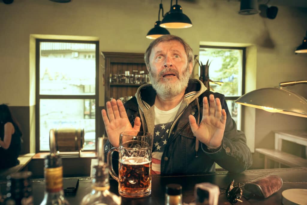 man with hands up at a bar with a pint of beer infront of him
