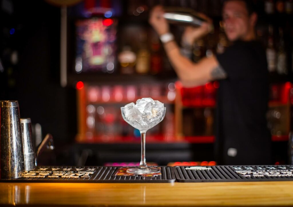 bartender using cobbler shaker in the background of a cocktail glass