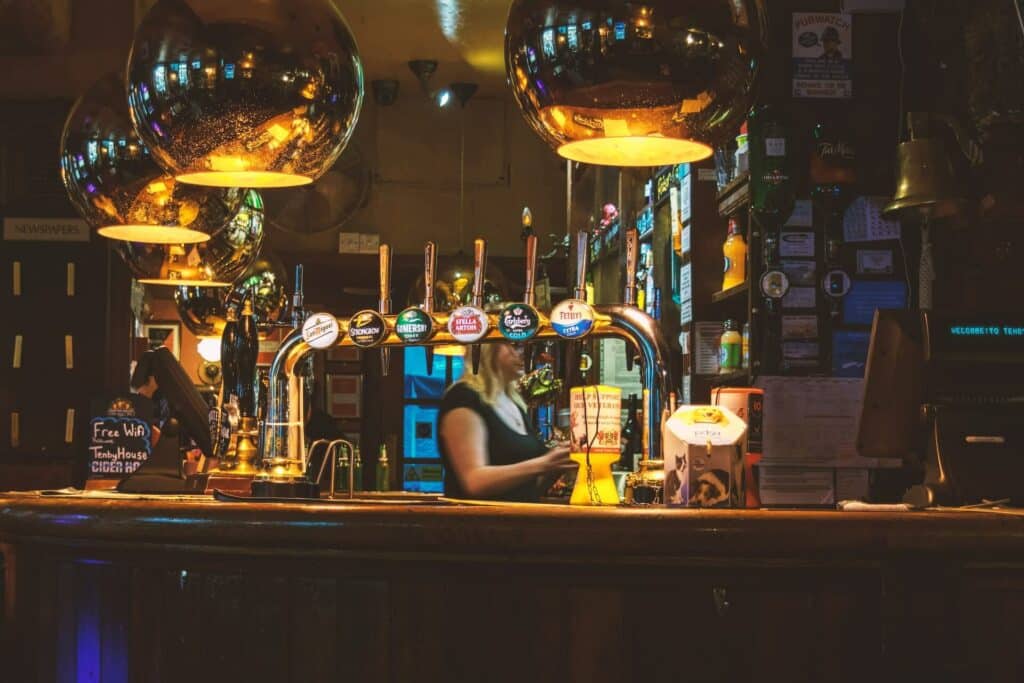 woman bartender behind the bar in a pub with beer brand logos on the pumps